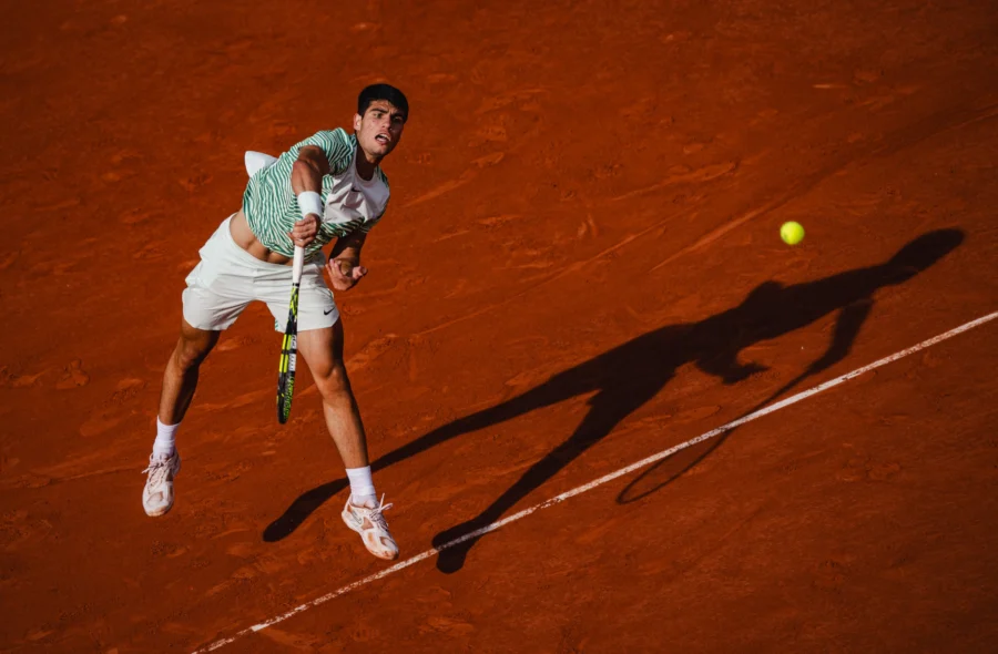 Tennis player serving on clay with a long evening shadow