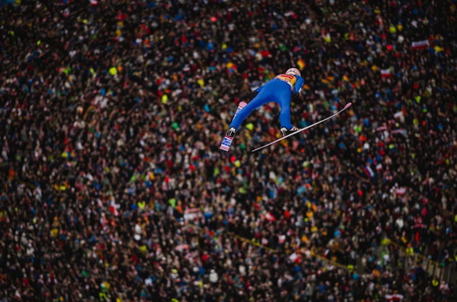 Ski jumper flying above a colourful crowd