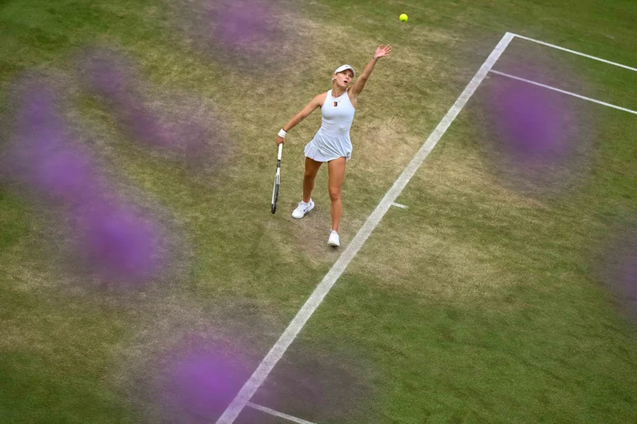Tennis player serving on grass, framed by flowers, Wimbledon 2025